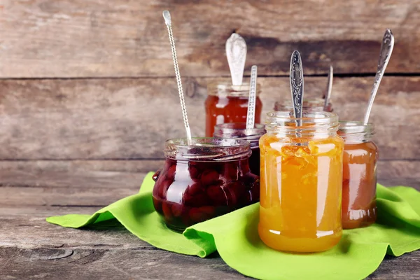 Jars of tasty jam with napkin on wooden background — Stock Photo, Image