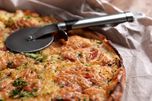 Tasty pizza with knife on paper close up — Stock Photo, Image