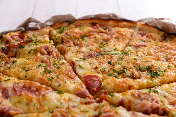 Pizza saborosa em papel sobre fundo de madeira — Fotografia de Stock