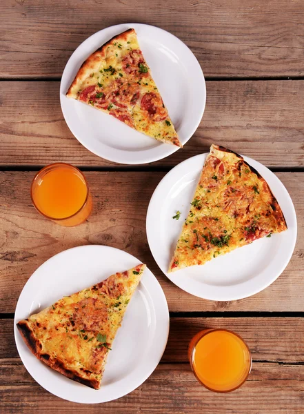 Tasty slices of pizza on plates with glasses of juice on wooden table — Stock Photo, Image