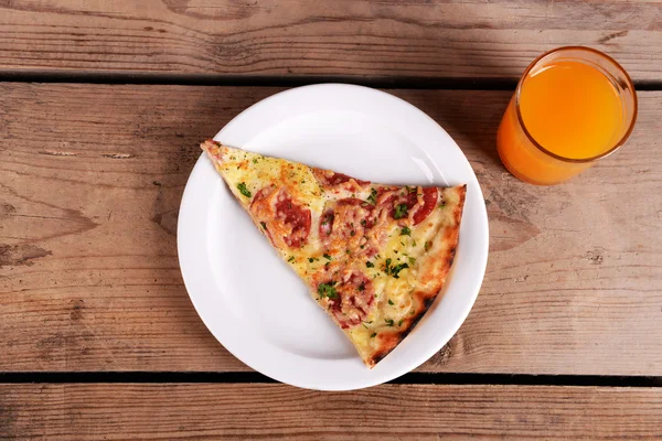 Gustosa fetta di pizza sul piatto con bicchiere di succo sul tavolo di legno — Foto Stock