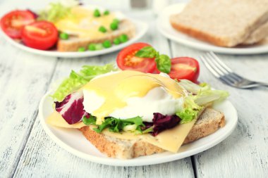 Yumurta Benedict ile tost ve ahşap masa üzerinde tabakta domates