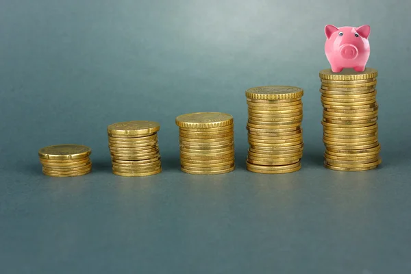 Hucha de cerdo de pie en la pila de monedas sobre fondo gris —  Fotos de Stock