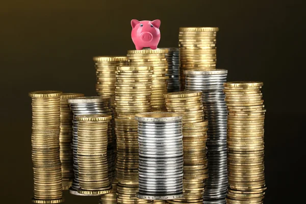 Hucha de cerdo de pie en la pila de monedas sobre fondo marrón —  Fotos de Stock