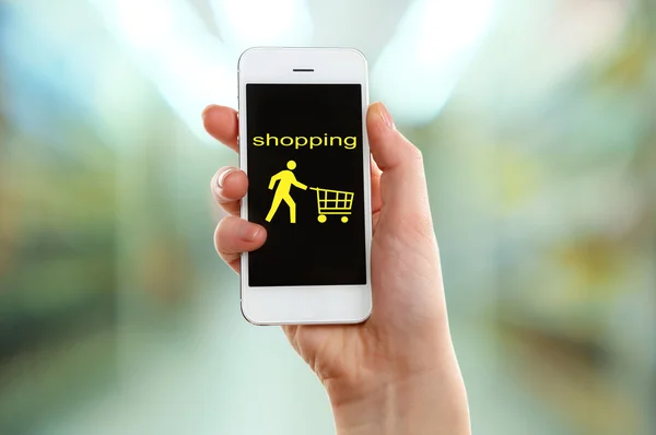 Mobile concetto di shopping. Mano che tiene il telefono cellulare per lo shopping su Internet su sfondo supermercato — Foto Stock