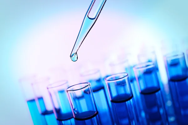 Pipette adding fluid to the one of test-tubes on bright background — Stock Photo, Image