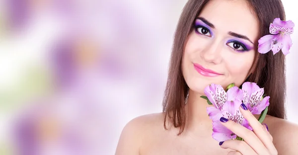 Mulher bonita com flor roxa em fundo de cor brilhante — Fotografia de Stock