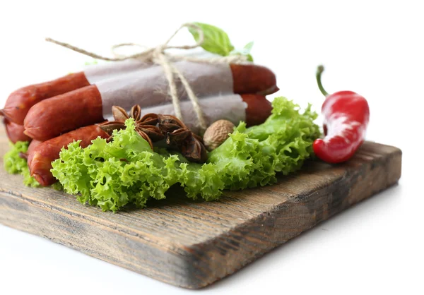 Smoked thin sausages  with lettuce salad leaves on wooden cutting board, isolated on white — Stock Photo, Image