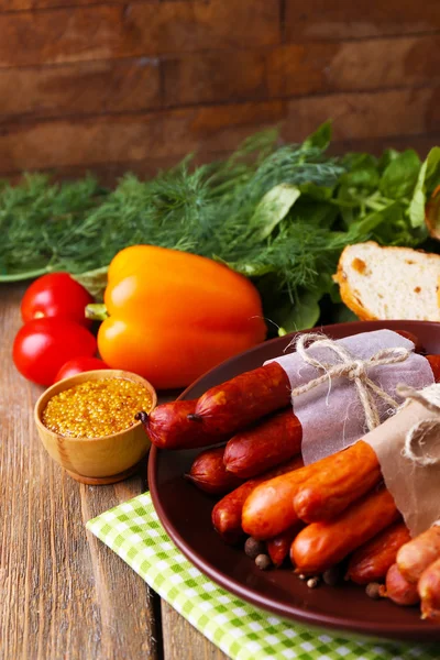 Assortment of thin sausages, and spices on plate, vegetables and bread on wooden background — Stock Photo, Image
