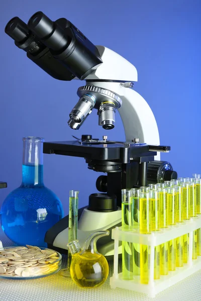 Mikroskop, ziarna i probówki na stole, na kolorowym tle — Zdjęcie stockowe