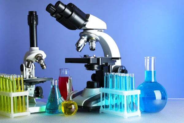 Microscopes and test tubes on table, on color background — Stock Photo, Image