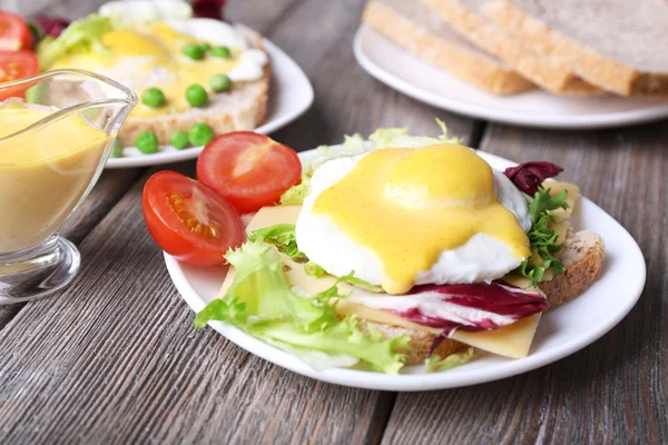 Toast with egg Benedict and tomato on plate on wooden table — Stock Photo, Image