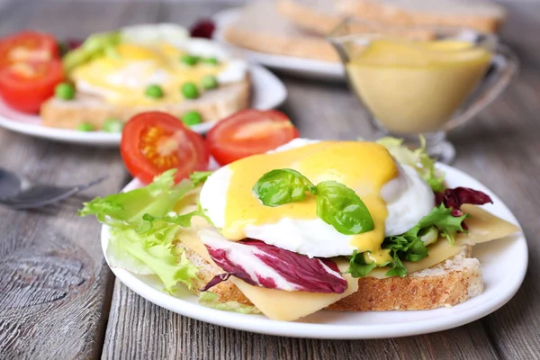 Toast with egg Benedict and tomato on plate on wooden table — Stock Photo, Image