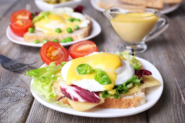 Toast with egg Benedict and tomato on plate on wooden table — Stock Photo, Image