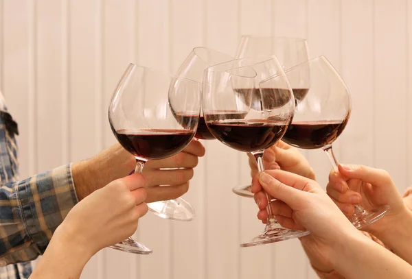 Copas de vino tinto en las manos sobre tablones de madera de color de fondo —  Fotos de Stock