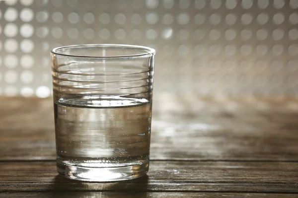 Glass of clean mineral water on wooden surface and lattice background — Stock Photo, Image