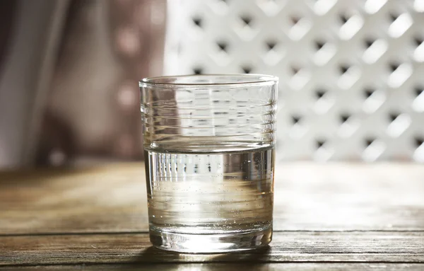 Glass of clean mineral water on wooden surface and lattice background — Stock Photo, Image