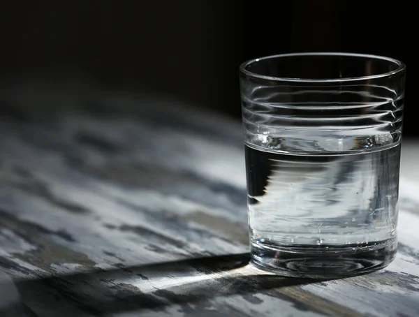Vidro de água mineral limpa na superfície de madeira de cor antiga e fundo escuro — Fotografia de Stock
