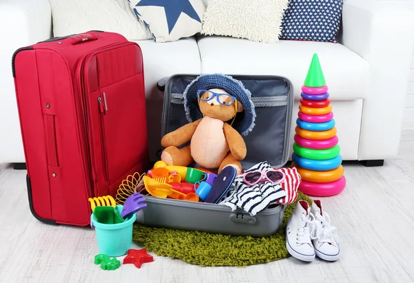 Suitcase packed with clothes and child toys on fur rug and white sofa background — Stock Photo, Image