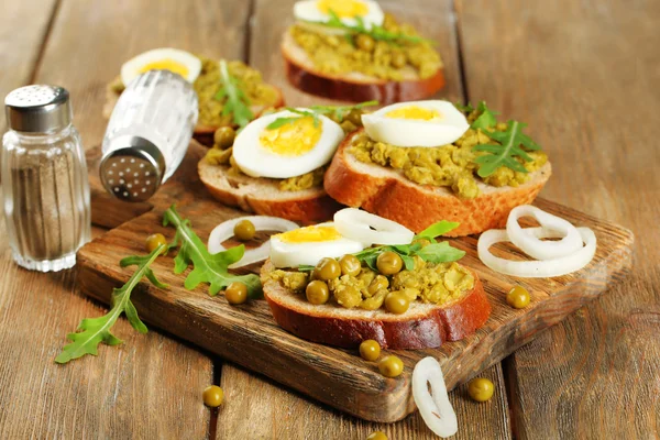 लाकडी प्लॅन पार्श्वभूमीवर हिरव्या पीस पेस्टसह सँडविच आणि कांद्याच्या रिंग आणि लिंबूसह उकळलेले अंडी — स्टॉक फोटो, इमेज
