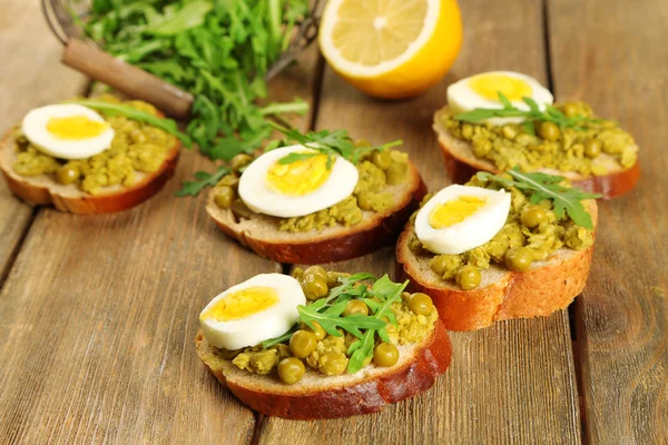 Sandwiches with green peas paste and boiled egg with herbs and lemon on wooden planks background — Stock Photo, Image