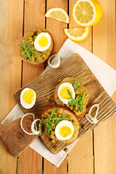 Sandwiches with green peas paste and boiled egg on cutting board with napkin on wooden planks background — Stock Photo, Image