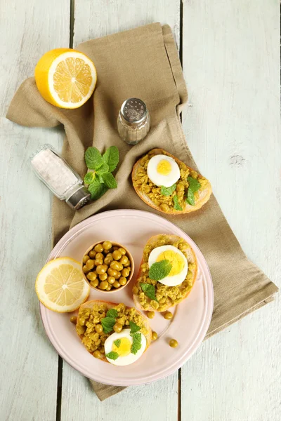 Sandwiches with green peas paste and boiled egg on plate with napkin on color wooden planks background — Stock Photo, Image