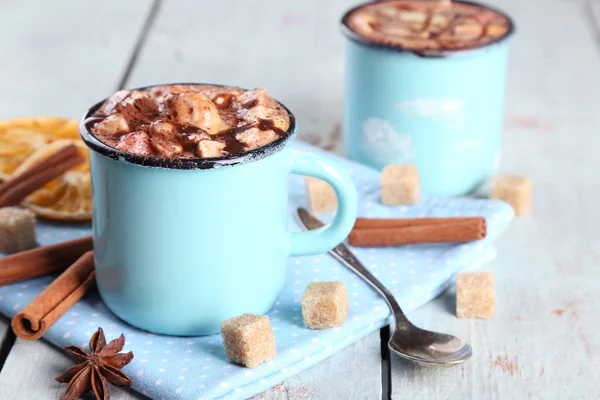 Tassen mit heißem Kaffee mit Marshmallow auf Serviette mit Klumpen Zucker, Zimt, Sternanis und getrockneter Orange auf farbigem Holztischhintergrund — Stockfoto