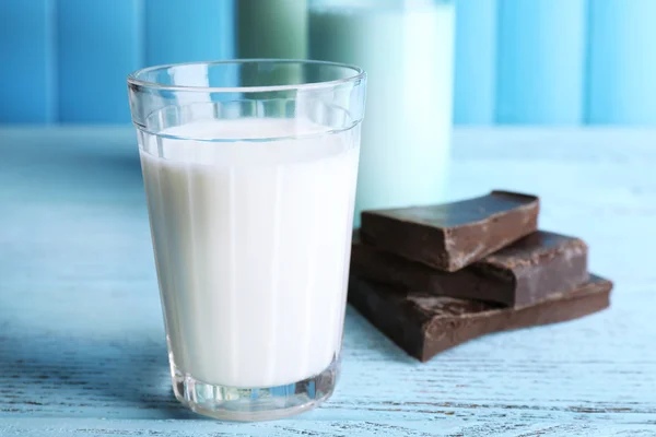 Bicchiere e bottiglie di latte con pezzi di cioccolato su sfondo tavole di legno colore — Foto Stock