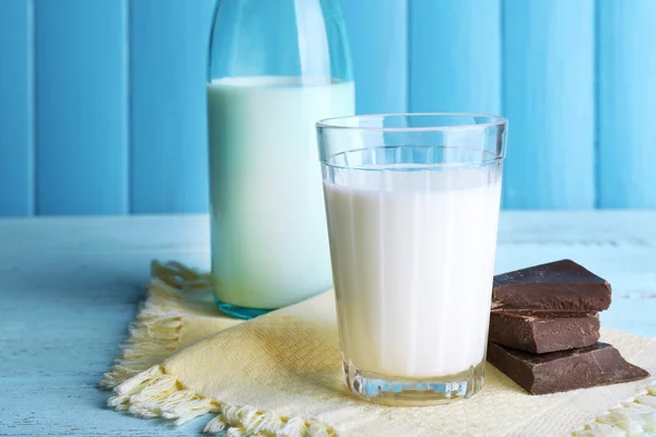 Glass and bottle of milk with chocolate chunks on color wooden planks background — Stock Photo, Image