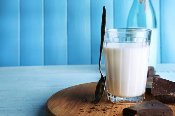 Glass and bottle of milk with chocolate chunks on cutting board and color wooden planks background — Stock Photo, Image