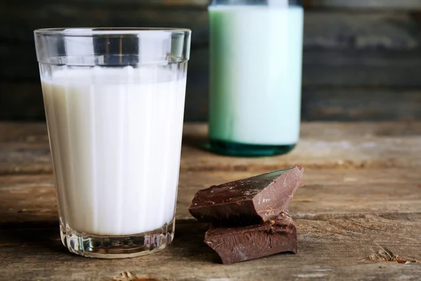 Glass and bottle of milk with chocolate chunks on rustic wooden planks background — Stock Photo, Image