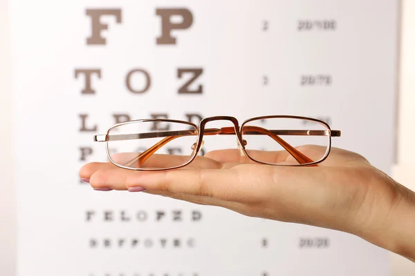 Okulary w kobieta dłoni na tle wykresu badanie wzroku — Zdjęcie stockowe