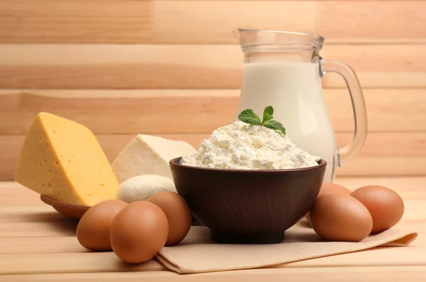 Queso cottage en tazón de barro con jarra de leche y huevos sobre tablones de madera de fondo — Foto de Stock