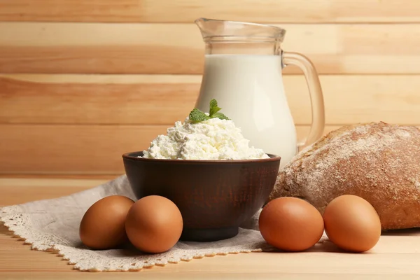 Queso de cabaña en tazón de barro con jarra de leche, pan y huevos sobre tablones de madera fondo — Foto de Stock