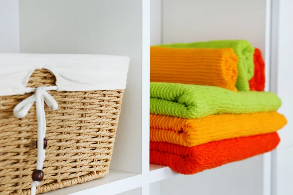 Colorful towels with wicker basket on shelf of rack background — Stock Photo, Image