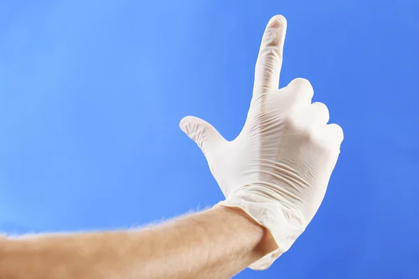 Main de médecin en gants stériles sur fond bleu — Photo