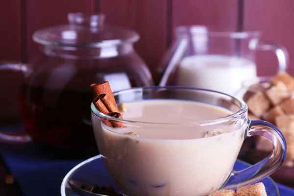 Té negro con leche y azúcar en bulto y especias en cristalería sobre fondo de tablones de madera de color — Foto de Stock