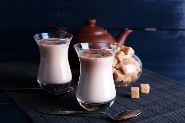 Černý čaj s mlékem v brýle a konvice s kusový cukr na bambusové mat a barvu pozadí Dřevěná prkna — Stock fotografie