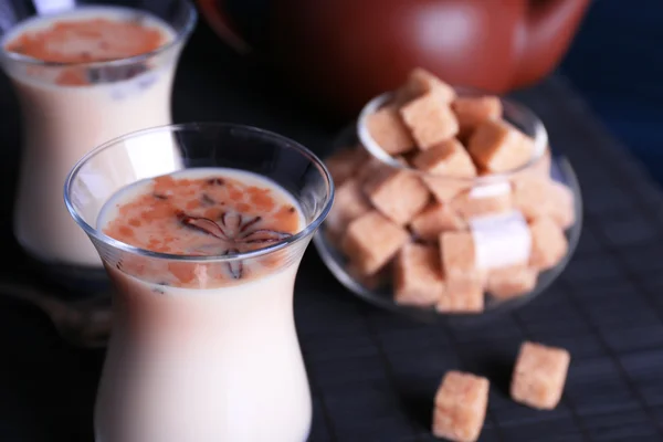 Chá preto com leite em copos e bule com açúcar de caroço no tapete de bambu e cor pranchas de madeira fundo — Fotografia de Stock