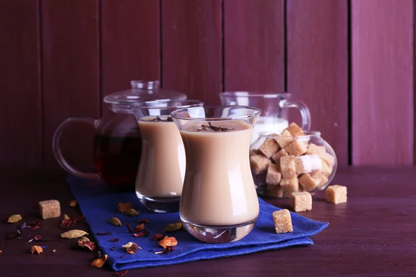 Schwarzer Tee mit Milch und Klumpen Zucker und Gewürzen in Gläsern auf farbigen Holzplanken Hintergrund — Stockfoto