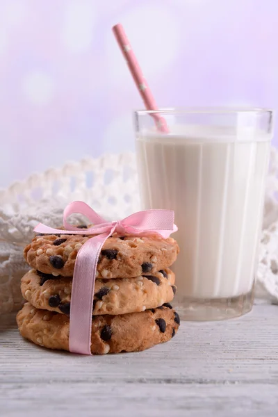 Biscoitos saborosos e vidro de leite na mesa de madeira a cores, no fundo brilhante — Fotografia de Stock