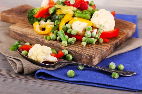 Verduras congeladas sobre tabla de cortar, sobre servilleta, sobre fondo de mesa de madera — Foto de Stock