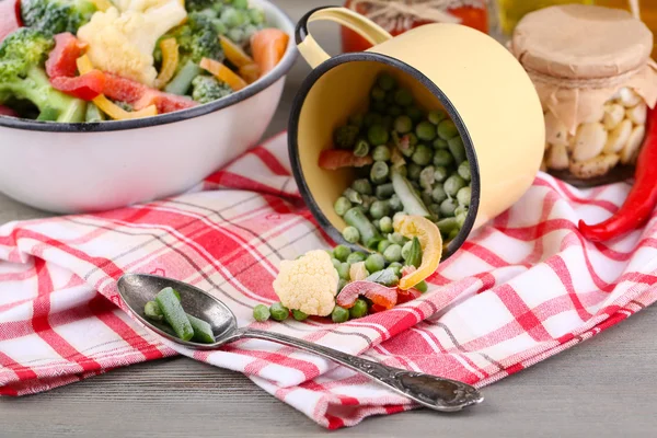 Légumes congelés dans un bol et une tasse sur une serviette, sur un fond de table en bois — Photo