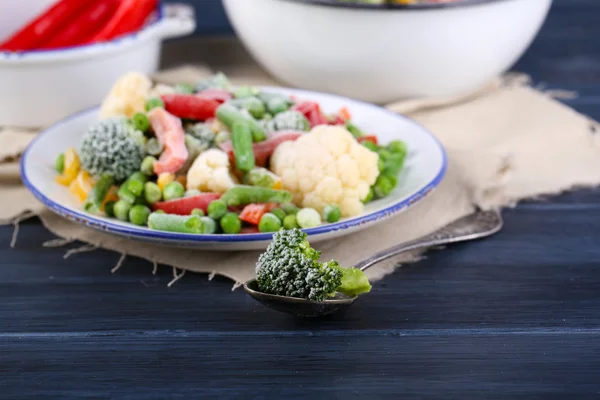 Замороженные овощи на тарелке на салфетке, на деревянном фоне стола — стоковое фото