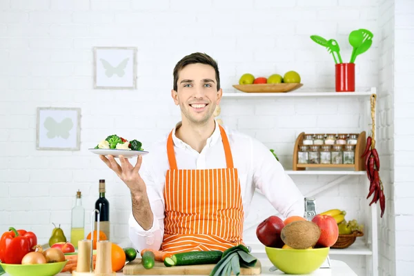 Человек за столом с различными продуктами и посудой на кухне на белом фоне стены — стоковое фото
