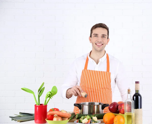 Uomo a tavola con diversi prodotti e utensili in cucina su sfondo bianco a parete — Foto Stock