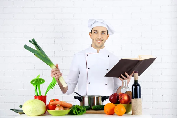 Chef a tavola con diversi prodotti e utensili in cucina su fondo bianco a parete — Foto Stock