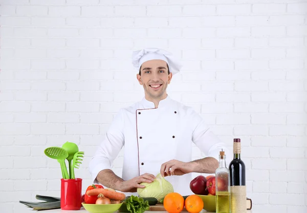 Chef a tavola con diversi prodotti e utensili in cucina su fondo bianco a parete — Foto Stock