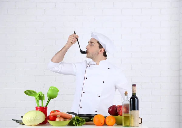 Chef a tavola con diversi prodotti e utensili in cucina su fondo bianco a parete — Foto Stock